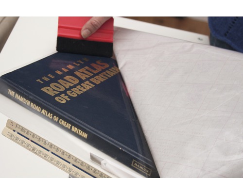 Buchschutzfolie wird mit einem Rakel auf einen Straßenatlas aufgebracht