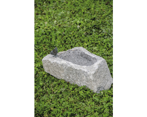 Vogeltränke aus Stein mit Schmetterling auf einer Wiese