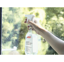 Eine Person sprüht Fensterfolien Montageflüssigkeit auf eine Scheibe.