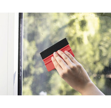 Hand reinigt Fenster mit einem Fensterwischer.