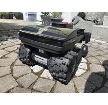 Schwarzer Rasenmähroboter mit groben Reifen auf Pflastersteinen