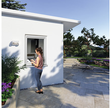 Szene eines modernen Gartenhauses mit Frau am Fenster und gepflastertem Außenbereich.