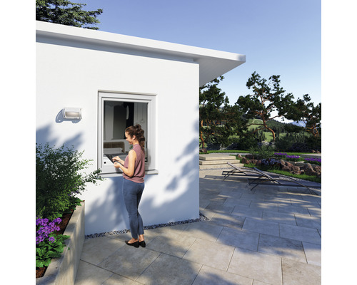 Szene eines modernen Gartenhauses mit Frau am Fenster und gepflastertem Außenbereich.