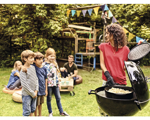 Eine Frau grillt im Garten mit Kindern und einem Kugelgrill.