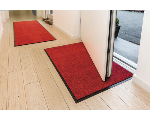 Eingangsbereich mit zwei roten Fußmatten mit schwarzem Rand auf Holzboden