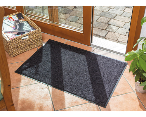 Graue Fußmatte vor einer Terrassentür auf Fliesenboden.