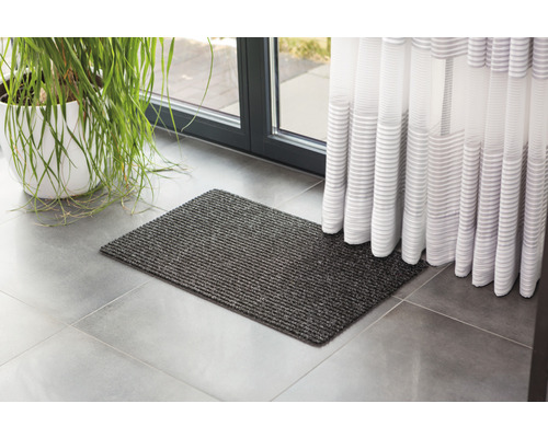 Grauer Fußabtreter vor einer Tür mit Vorhang und einer Zimmerpflanze.