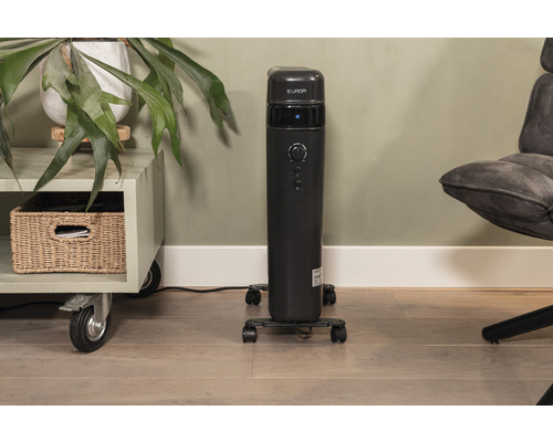 Schwarzer Säulenheizkörper auf Rollen neben einem Regal und einem Stuhl