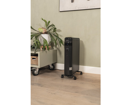 Schwarzer Elektro-Heizkörper mit Rollen in einem Wohnraum neben einem Schrank und einer Zimmerpflanze.