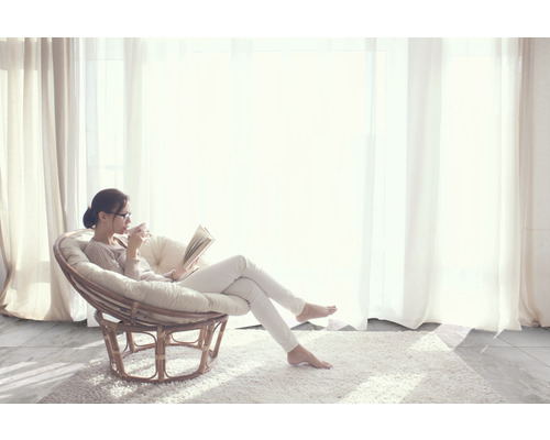 Frau liest Buch in einem Rattansessel auf einem Teppich vor einem Fenster
