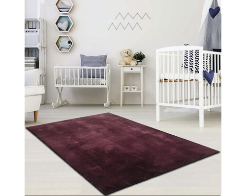 Ein Kinderzimmer mit einem bordeauxfarbenen Teppich, Kinderbetten und Regalen.