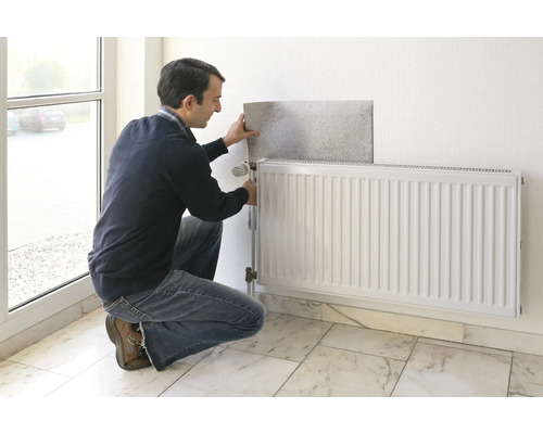 Mann montiert eine Heizkörperreflexionsfolie hinter einem Heizkörper an einer Wand