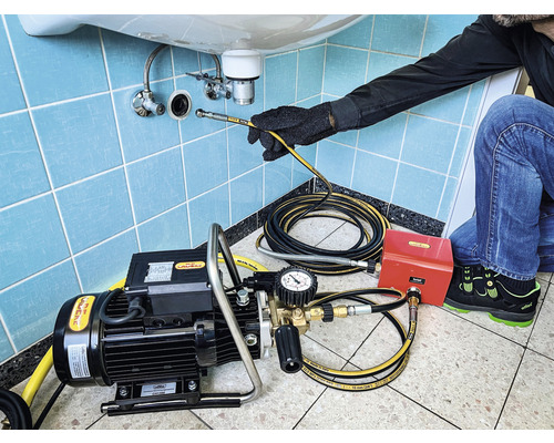 Ein Handwerker benutzt eine Rohrreinigungsmaschine unter einem Waschbecken, um eine Verstopfung zu beseitigen.