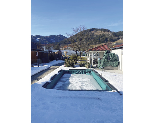 Eingefrorener Swimmingpool im Wintergarten mit Schnee bedeckt.