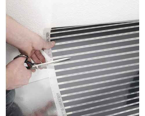 Eine Person schneidet eine Fußbodenheizungsmatte mit einer Schere zu.