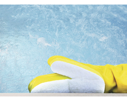 Gelbe Gummihandschuhe liegen auf einer Beckenumrandung vor blauem Wasser.