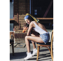 Eine junge Frau mit Kopftuch sitzt mit einem Getränk auf einem Stuhl.