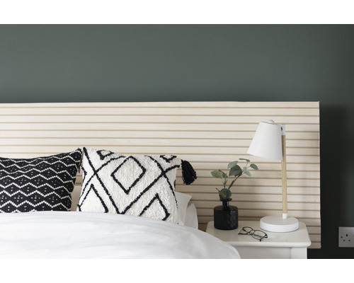 Schlafzimmerszene mit Bett, Nachttisch, Lampe und dekorativen Kissen.