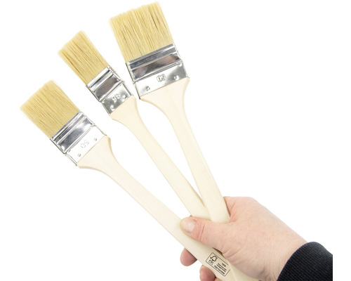 Eine Hand hält drei Pinsel mit Holzgriffen und Naturborsten