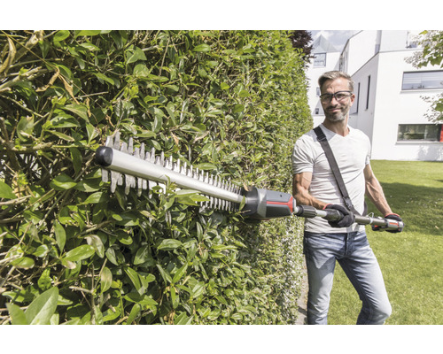 Mann schneidet Hecke mit einer Heckenschere im Garten.