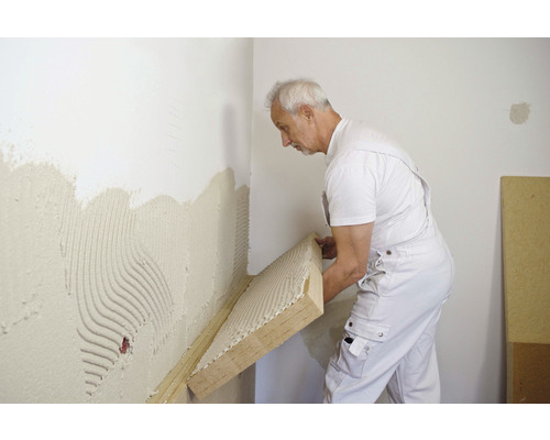 Mann befestigt Dämmplatte an Wand mit Kleber