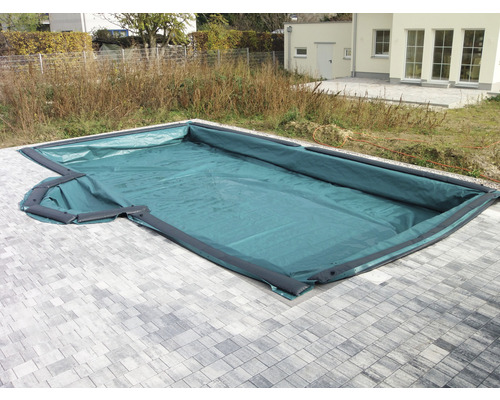 Winterabdeckplane für Pool KWAD 6x3 m Absenkung 70 cm grün Abgedecktes Schwimmbecken im Außenbereich mit grauer Steinumrandung und umliegendem Garten