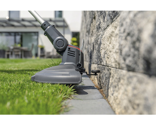 Rasentrimmer schneidet Gras an einer Steinmauer