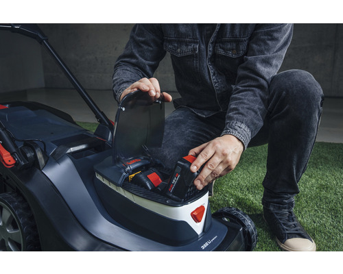 Eine Person legt einen Akku in einen Akku-Rasenmäher.