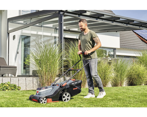 Ein Mann mäht Rasen mit einem Rasenmäher der Marke AL-KO in einem Garten.