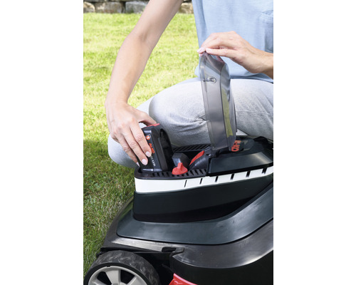 Eine Person setzt einen Akku in einen Rasenmäher ein.