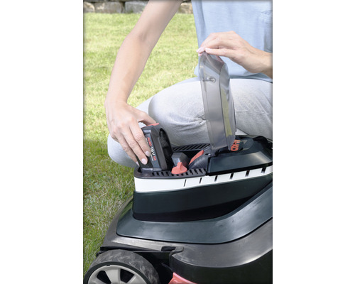 Eine Person setzt einen Akku in einen Rasenmäher ein.