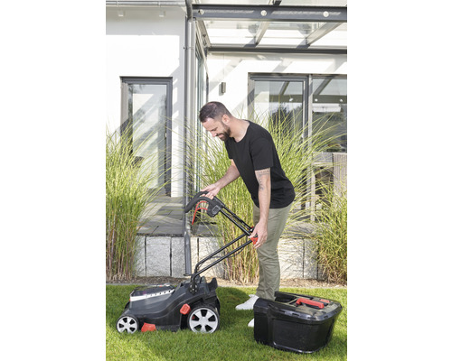 Mann bedient einen Rasenmäher mit Fangkorb im Garten.