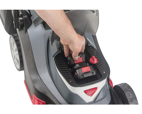Aufsicht auf einen Rasenmäher, in dessen Batteriefach eine Hand zwei Akkus einsetzt.