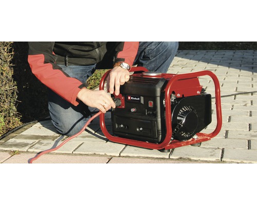 Ein Mann schließt ein rotes Stromkabel an einen Generator der Marke Einhell an.