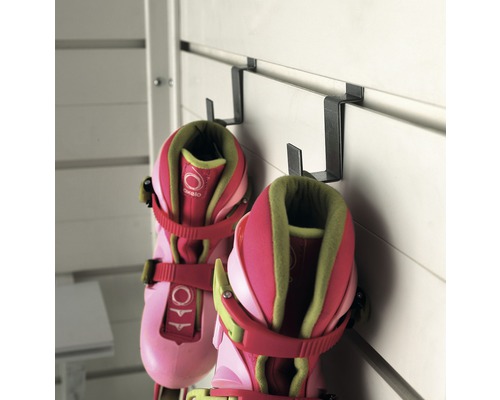 Ein Paar Inlineskates hängt an Metallhaken an einer weißen Wand