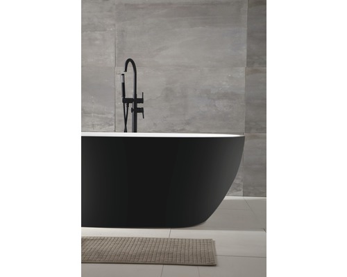 Freistehende schwarze Badewanne mit Armatur und Badteppich in einem Badezimmer mit Fliesenwand