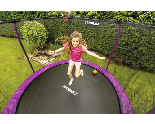 Mädchen springt auf Trampolin mit Sicherheitsnetz und Basketballkorb im Garten
