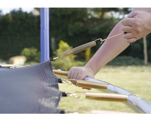 Detailaufnahme einer Person, die eine Feder an einem Trampolin befestigt.