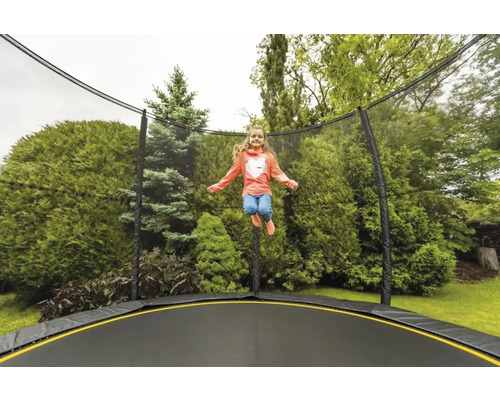 Mädchen springt auf einem Gartentrampolin mit Sicherheitsnetz vor grünen Büschen