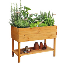 Hochbeet aus Holz mit verschiedenen Kräutern und Gemüsesorten sowie Ablagefläche mit Gartenzubehör
