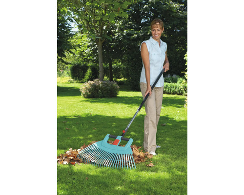 Frau harkt Laub mit einem Fächerbesen im Garten.