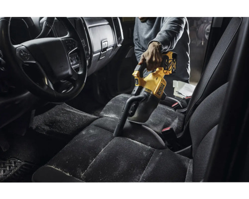 Eine Person saugt mit einem gelben Handstaubsauger von DeWalt den Innenraum eines Autos.
