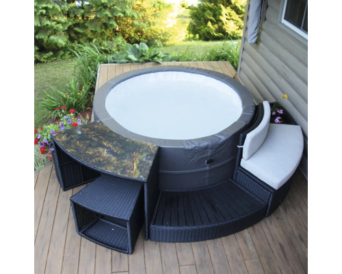 Runder Whirlpool mit Umrandung aus Rattanmöbeln auf einer Holzterrasse
