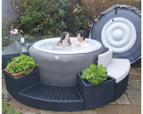 Szene mit einem aufblasbaren Whirlpool im Garten, umgeben von einer Sitzgruppe und zwei Personen im Wasser.