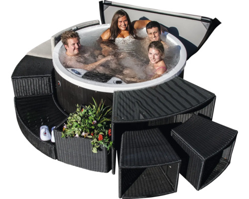 Runder Whirlpool mit schwarzer Verkleidung, umgeben von modularen Rattanmöbeln und entspannten Personen
