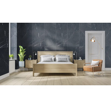 Schlafzimmer mit Bett, Nachttischen, Sessel und Wandfliesen in Marmoroptik