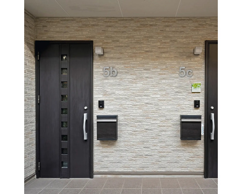 Eingangsbereich mit zwei Haustüren, Briefkästen und Hausnummern an einer Steinwand
