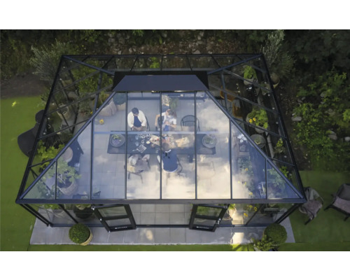 Außenansicht eines Gewächshauses mit Pflanzen und einer Gruppe von Personen, die an einem Tisch sitzen.