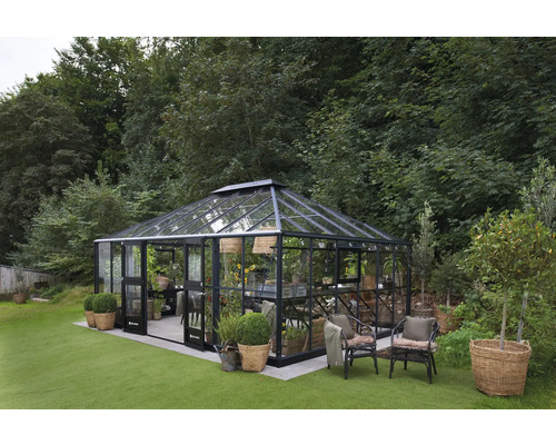 Gewächshaus Juliana Grand Oase inkl. Sicherheitsglas 3 mm 439 x 583 cm anthrazit Gewächshaus aus Glas und Metall im Garten mit Pflanzen und Möbeln.