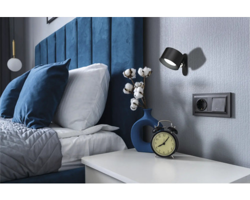 Schlafzimmer mit Bett, Nachttisch, Wandleuchte und Steckdose